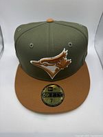Front view of olive green and brown New Era 59FIFTY hat with Toronto Blue Jays logo and size 7 1/2 sticker on brim.