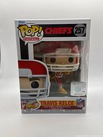 Front view of Funko Pop! Travis Kelce vinyl figure in packaging, showing number 257, Chiefs branding, and NFL holographic sticker.