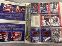 Open binder showing multiple hockey cards with blue ink autographs and limited edition numbering in plastic sleeves.