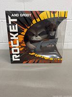 Front view of sealed Rocket and Groot vinyl collectible in box showing Rocket character with weapon.
