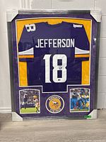 Full frontal view of the framed purple Vikings jersey with gold matting and two action photos below.