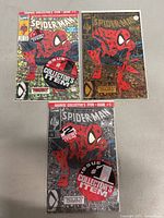 Overview of all three Spider-Man #1 comics showing one loose and two sealed in bags, displaying different cover variants including a gold foil variant.