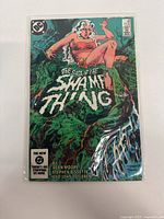 Front cover of The Saga of The Swamp Thing issue #25 in protective sleeve, showing the title, colorful swamp artwork and female character.