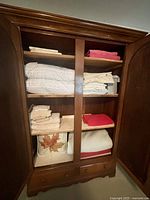 Open armoire showing three cedar shelves stacked with folded linens and the two small bottom drawers.