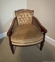 Front view of the mid century armchair showing tufted velvet upholstery, cane sides and wooden arms and legs.