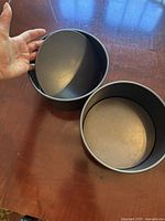 Two 8-inch round cake pans stacking with loose bases visible inside on a wooden surface, showing the pans' depth and size relative to a hand.