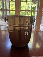 Front view of large reflective metal champagne bucket showing cylindrical shape and side handle.