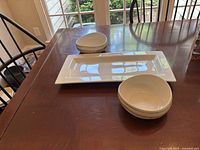 Pair of medium-sized white china bowls and white rectangular serving tray on a wooden table.