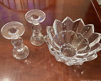 Photo showing a clear Mikasa crystal bowl with petal-shaped scalloped edges and two clear glass candlestick holders with rounded bases on a wooden surface.