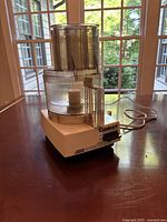 Cuisinart food processor seen from a side angle showing the work bowl, handle, lid with feeding chute, and base motor unit with power cord on a wooden table.