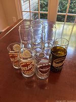 Photo of 4 tall Smith glasses and 5 small vintage-style juice glasses with various printed logos and texts.