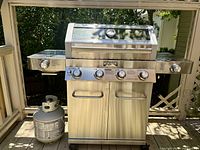 Front view of grill with lid closed showing stainless steel finish, control knobs and propane cylinder attached