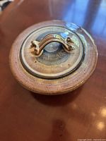 Top view of pottery casserole lid showing curved textured handle and detailed surface pattern.