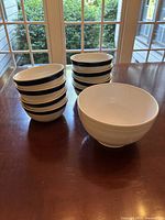 Photo of one large white serving bowl and eight smaller white soup bowls stacked in two stacks with visible black stripes on the small bowls.