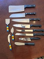 Photo of 10 cutting utensils on a wooden surface including butcher knives, serrated knives, cheese cutting utensils and spreaders.