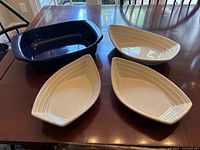 Four open casserole dishes displayed on a wooden table, including one cobalt blue Chantal casserole dish and three cream-colored boat-shaped dishes.