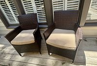 Pair of dark brown resin wicker patio chairs on wood deck, each with removable beige seat cushion