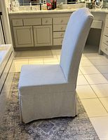 Side profile of beige linen Parsons chair showing the padded seat, high backrest, and skirted bottom.