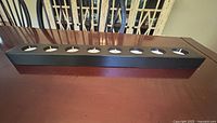 Long rectangular black metal holder on a wooden surface with 8 white tea lights placed inside.