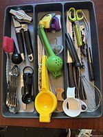 Top-down view of assorted kitchen small utensils and tools organized in a gray divided plastic tray
