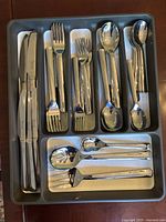 Full view of Robert Welch stainless steel flatware pieces arranged in a gray plastic tray, showing knives, forks, spoons, and serving utensils.