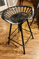 Single black metal tractor seat stool showing seat design and leg structure