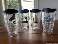 Photo showing four 16oz Tervis tumblers with beach-themed designs and black lids, including pelican, palm trees, sailboat, and dolphins.