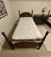 Close view of the antique wooden twin bed frame showing carved posts and new mattress with quilted white floral design