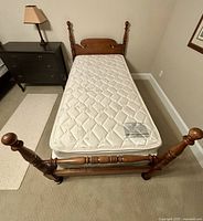 Antique wooden twin bed frame with turned posts, new mattress and box spring set up in a room.