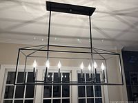 Black farmhouse rectangular light fixture with 8 candle bulbs illuminated, mounted on ceiling in living space.