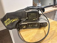 Left side view showing belt sander body, dust bag with Sears Craftsman logo, model label
