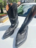 Pair of black leather cowboy boots upright on hood of vehicle
