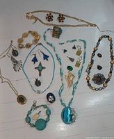 Photo showing assortment of various costume jewelry items spread out including multiple necklaces, bracelets, earrings, pendants, and brooches.