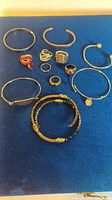 Overview photo showing assortment of bracelets and rings on blue surface
