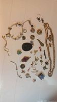 Full overview of assorted costume jewelry pieces laid out on white surface showing variety of pendants, earrings, bracelet, necklace, and pins.