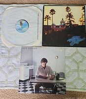 Three vinyl records shown: Eagles 'Hotel California' with cover, Don Henley 'I Can't Stand Still' album cover, and Eagles vinyl record partially in sleeve.