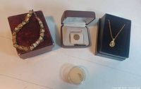 The full lot showing the 10k gold bracelet, the 10k gold opal pendant necklace, a small gold charm in plastic box, with jewelry boxes.
