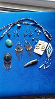 Multiple Indigenous American tribal style jewelry items on blue background including earrings, necklaces, rings, and pendants with stone and bead materials.