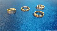 Four men's rings on blue fabric background showing variety including spoon ring and rings with clear stones