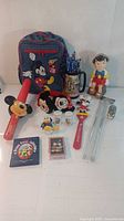 Wide shot of assorted Disney collector items including backpack, figurines, and stationery on white surface.