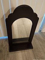 Front view of dark wood framed arched wall mirror with base on a floor.