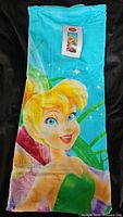 Full view of the folded Tinkerbell beach towel showing large detailed print of Tinkerbell with turquoise background.