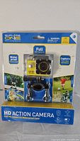 Front view of the sealed original packaging showing the yellow black HD Explore One action camera in waterproof case and included mounts.