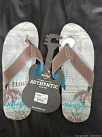 Top view showing the graphic printed footbed and tan fabric straps with tags attached indicating brand new condition.