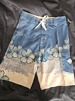 Full view of the blue and beige Hard Rock Cafe boardshort with hibiscus floral print, lace-up front, and cargo pocket.