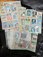 Photo showing a wide assortment of baseball cards inside plastic sleeves in binders and loose piles on a black surface.