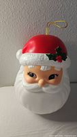 Front view of plastic Santa head decoration, showing face and red hat with holly detail.