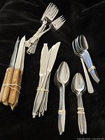 Photo showing assorted flatware including knives with wooden handles, stainless steel forks, knives, tablespoons, and teaspoons bundled separately.