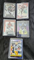 Front view of five football trading cards in protective sleeves showing images of players in action