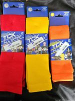 Three pairs of TCK All Sport socks in red, yellow, and orange, showing the front packaging with size L indicated.